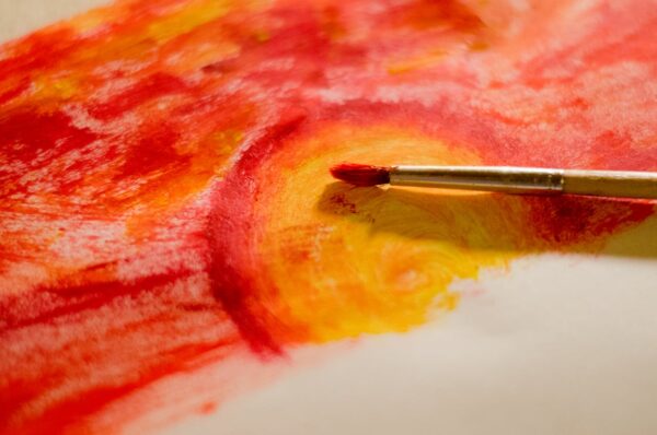 A dynamic abstract painting showcasing vibrant red and yellow hues with a paintbrush.